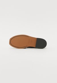 Semelle en cuir avec un talon en caoutchouc noir lisse et une base en cuir bruni, cousue, présentant un détail de logo embossé.