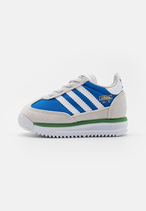 Baskets Adidas SL ’72 bleu et blanc avec bande verte sur la semelle, lacets blancs et empiècements en daim, vues du côté extérieur.