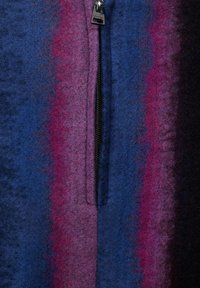 Veste zippée en tissu feutré avec des rayures dégradées de bleu, violet et noir. Elle dispose d'une fermeture éclair centrale avec des accents métalliques.