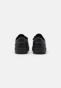Black leather sneakers with a textured surface, rounded toe, and rubber soles; features subtle red accents near the heel and sleek design.