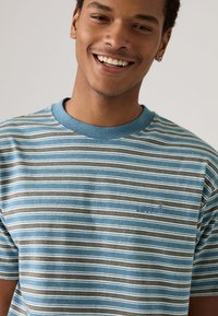 Striped short-sleeve t-shirt in blue, brown, and white. Features a crew neck and a small logo on the chest. Soft, cotton material.