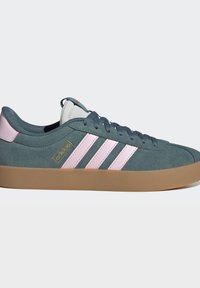 Baskets basses en daim bleu-gris avec des bandes roses Adidas et une semelle en gomme, vues de profil sur fond uni.