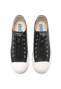 Zapatillas de lona negras con punteras de goma blanca, cordones negros planos y una etiqueta de marca en la plantilla. Diseño minimalista con acentos en contraste.