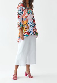 Blouse colorée à motif floral, coupe oversize et manches trois-quarts. Associée à un pantalon blanc à jambes larges et des sandales à talons carrés roses.