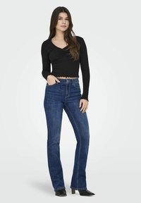 Maglietta nera a maniche lunghe con dettagli arricciati e orlo a scallop, abbinata a jeans a zampa blu. Tessuto morbido con vestibilità casual.