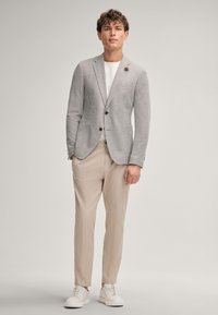 Blazer a righe in tessuto grigio e bianco con due bottoni, abbinato a pantaloni beige e sneaker bianche. Presenta un dettaglio di fazzoletto nel taschino.
