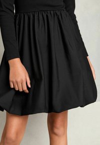Schwarzes Kleid mit enganliegendem Oberteil und plissiertem Rock. Lange Ärmel und geraffter Taillenbund, aus glattem Stoff gefertigt. Einfaches, einfarbiges Design.