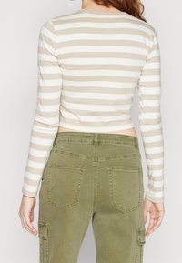 Beige and white striped crop top with long sleeves, paired with olive green cargo pants featuring back pockets and side cargo pocket.