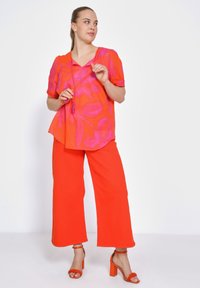 Heldere roze en oranje bloemenpatroon top met korte mouwen, gecombineerd met levendige oranje wijde broekspijpen en sandalen met hakken en bandjes.