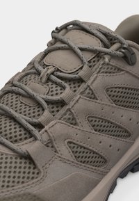 Μπεζ αθλητικό παπούτσι με αναπνεύσιμο δίχτυ και επικαλύψεις από σουέντ, ασφαλισμένο με στρογγυλά κορδόνια με σχέδιο που περνούν μέσα από υφασμάτινους βρόχους και πόρπη.