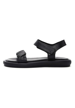 Sort flad sandal med polstret sål, forreste rynket rem og justerbar anklerem med Velcro-lukning.