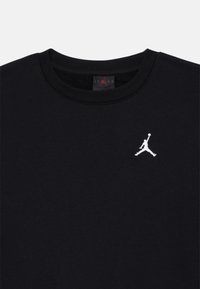 Svart bomull T-skjorte med rund hals og en hvit brodert Air Jordan-logo på venstre bryst. Myk tekstur, minimalistisk design.