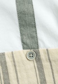 Tote en coton avec une partie supérieure blanche, une sangle en toile rayée verte, un bas beige avec des rayures grises et un bouton rond gris en détail.