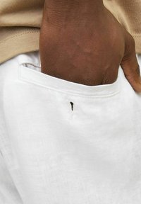 Białe lniane spodnie z małym czarnym przeszyciem na kieszeni bocznej, zestawione z jasnobeżowym materiałem na górze.