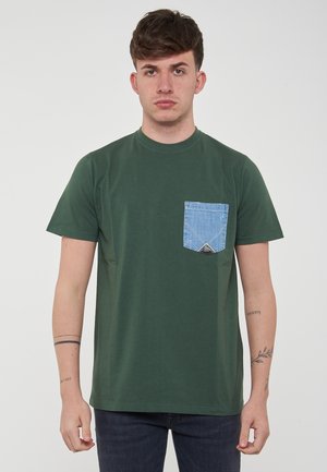 Groene katoenen t-shirt met een ronde halslijn en korte mouwen, met een blauwe denim zak op de linkerborst met een driehoekige accent.