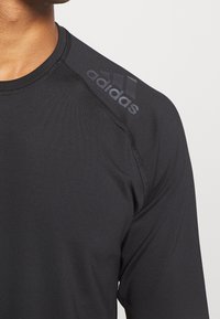 Svart atletisk långärmad tröja med rund halsringning, flatlock-sömmar och en tonad Adidas-logotyp på axeln. Slät, lättviktig tyg.