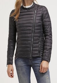 Chaqueta acolchada negra con cuello alto, cierre frontal asimétrico, bolsillos delanteros y puños acanalados. Textura lisa y brillante.