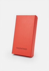 Caja de papel roja Valentino, forma rectangular, acabado mate, con el nombre de la marca en texto negro en la parte frontal.