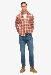 Rot-weißer kariertes Hemd mit Button-Down-Kragen, kombiniert mit blauen Jeans und hellbraunen Schnürschuhen. Legere Outfit mit strukturierter Passform.
