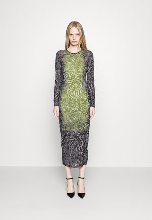 Langermet kjole med et svart og grønt zebra mønster, gjennomsiktig stoff, tettsittende silhuett og midilengde, kombinert med svarte ankelsandaler.