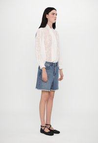 Blusa bianca trasparente con motivo floreale, abbinata a una gonna di jeans azzurri chiari con orlo sfilacciato e ballerine nere con dettagli borchiati.
