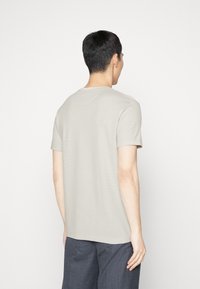 Jasnoszara krótka koszulka z krótkim rękawem, okrągłym dekoltem, prążkowaną teksturą i luźnym krojem, zaprezentowana z tyłu.