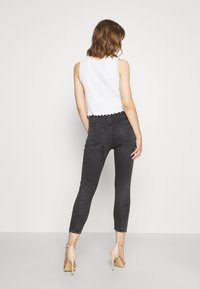 Top blanco sin mangas con dobladillo con forma de ola, combinado con jeans negros de tiro alto y sandalias de tacón nude. Texturas suaves y diseño ajustado.