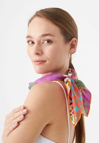 Zijden sjaal in levendige kleuren, met bloem- en geometrische patronen. Om de hals gebonden met een strik, waarbij de glanzende textuur wordt benadrukt.