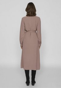 Dlouhé, mauve šaty s páskem v oblasti pasu, dlouhými rukávy a volným střihem. Texturovaná látka a délka šatů pod kolena dokonale doplňují design.