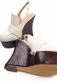 Scarpe a zeppa slingback bianche in pelle con tacco in legno scuro texture e accenti silver. Superficie liscia con design a punta arrotondata.