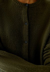 Dunkelgrüner Cardigan aus weichem Stoff, mit einem gerippten runden Halsausschnitt, einer Vorderknopfverschluss mit vier schwarzen Knöpfen und langen Ärmeln.