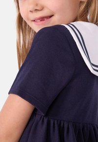 Φόρεμα από βαμβάκι σε ναυτικό μπλε με κοντά μανί κια, φούστα με πιέτες και λευκό γιακα ναύτη με ρίγες σε ναυτικό μπλε.