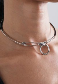Collier ras du cou en argent au design incurvé, mettant en avant des fils métalliques entrelacés et un accent en forme de cercle au centre.