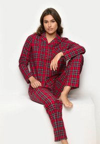 Conjunto de pijama de cuadro rojo hecho de tela suave, con una parte superior de botones y pantalones de corte relajado. Presenta patrones de cuadros en verde y negro.