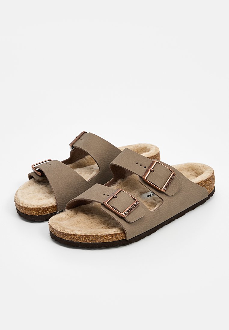 Sandales brunes à deux brides avec boucles métalliques, doublure en fourrure douce et semelle en liège. Les brides texturées offrent confort et stabilité.