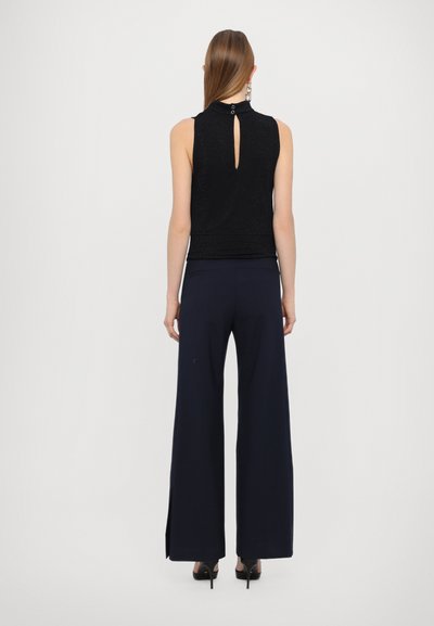 Zwarte mouwloze top met een opening aan de achterkant, gecombineerd met marineblauwe wijde broek met zijsplitten. Hoge hakken maken de look compleet.