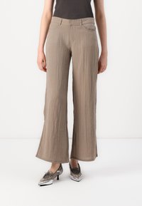 Beige wide-leg trousers in crinkled fabric, featuring a mid-rise waist and front pockets, paired with metallic-gray pointed shoes.