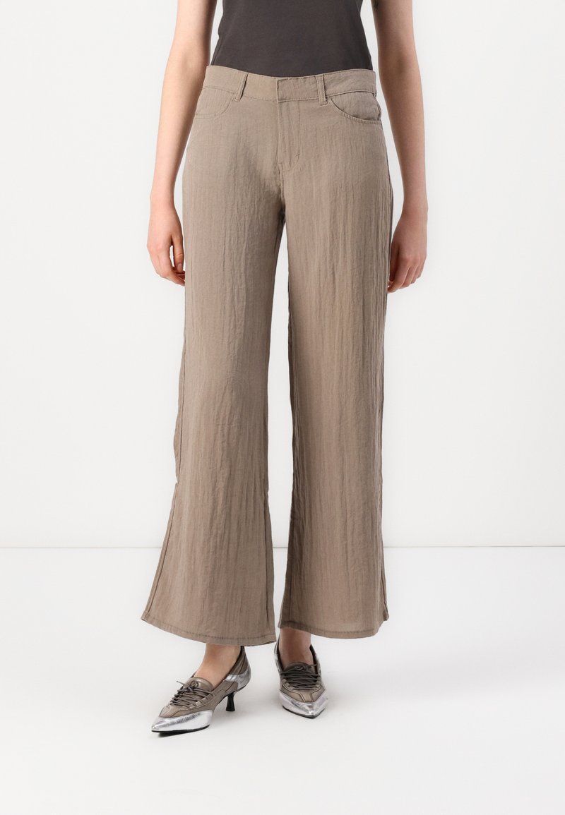 Beige wide-leg trousers in crinkled fabric, featuring a mid-rise waist and front pockets, paired with metallic-gray pointed shoes.