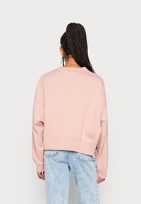 Ljust rosa, kort sweatshirt tillverkad av mjukt material med droppade axlar och vida ärmar, kombinerad med högmidjade ljusblå jeans.