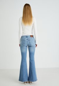 Pantalones vaqueros acampanados de color azul claro con una cintura de altura media, material de mezclilla, dos bolsillos traseros y un parche de cuero marrón en la cinturilla.