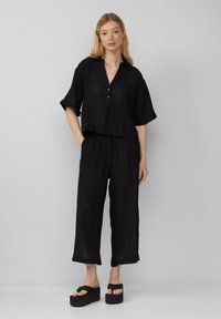 Zwarte cropped shirt met een kraag en drie knopen, gecombineerd met zwarte wijde broek. Heeft een gestructureerde stof en gelaagde platform sandalen.