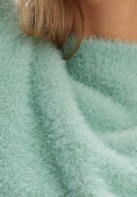 Pull vert menthe, duveteux, avec un tissu doux et texturé. Le matériau semble chaud et confortable, avec une coupe ample et fluide.