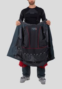 Skidjacka med mörkblå utsida, röda detaljer och svart insida med rutmönster. Har flera fickor och justerbara remmar.