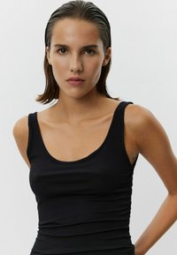Čierny rebrovaný top bez rukávov s okrúhlym výstrihom a tenkými ramienkami. Mäkka textura, priliehavý strih a elastický materiál. Žiadne vzory ani akcenty.