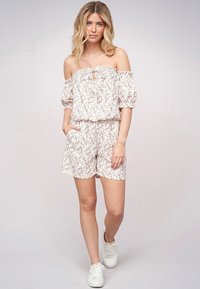 Blomstrete off-shoulder romper med korte ermer og elastisk midje. Har en lys rosa bunn, lite blomstermønster og sidelommer.