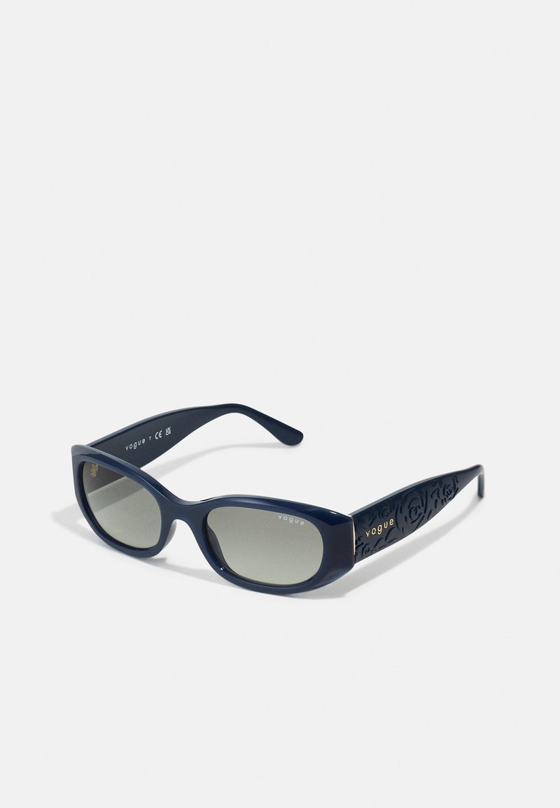 Navy sunglasses with a chunky frame, gradient gray lenses, and intricate floral pattern on the temples. Logo "vogue" in gold on the side.