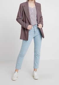 Tjekket blazer i bordeaux og hvid, lagd over en stribet skjorte, parret med lyseblå jeans og hvide sneakers. Skræddersyet pasform.