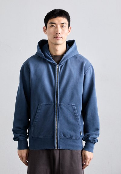 Sudadera con cremallera de color azul oscuro, fabricada en una mezcla de algodón, que presenta una gran capucha, dos bolsillos frontales y puños acanalados en las mangas y el dobladillo.