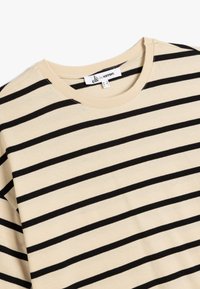 Beige bomuldsbluse med sorte vandrette striber, rund halsudskæring og et mærke med teksten "ole by ketton." Blød og let tekstur.