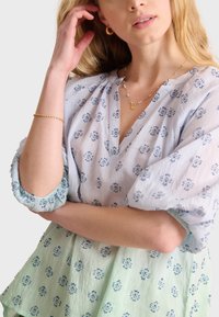 Blusa bordada en azul claro y verde con escote en V, mangas abullonadas y un corte relajado. Presenta patrones florales y detalles fruncidos.